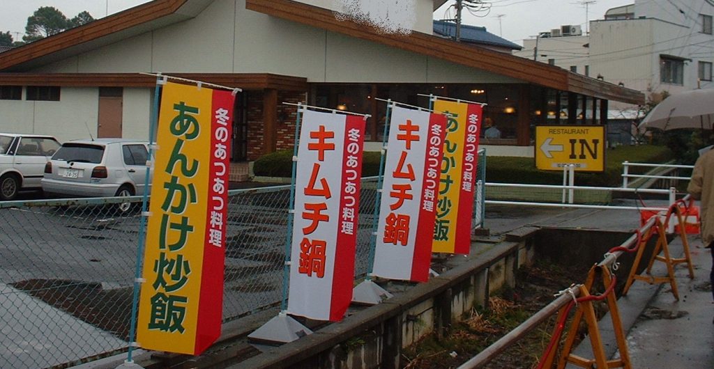 繁盛立地の紐解き　繁盛する駐車場「使いやすい駐車場８つの条件」　条件5駐車場は、その入口も出口も見えなければいけない　写真1のぼり旗が邪魔をして、駐車場の入口や出口が見えない事例